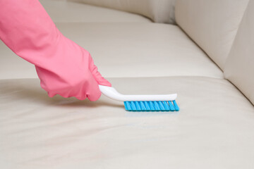 Cleaner hand in rubber protective glove brushing light gray leather sofa with professionally brush....