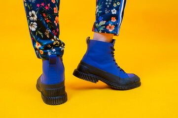 Fashion woman's legs in colorful pants and blue boots over yellow background