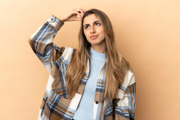 Young caucasian woman isolated on beige background having doubts while scratching head