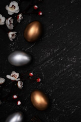 Golden and silver Easter eggs with flower on black background.