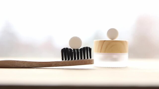 Side view of white toothpaste tablets with fluoride. Dental care concept. Natural ingredients, side view of bamboo toothbrush with white toothpaste tablet on brushes, blurred jar on background.