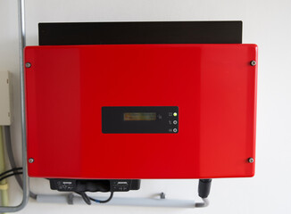 Close up of a red solar power inverter mounted to a white wall. Omvormer for solar energy to 230V power grid.