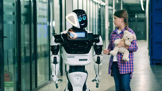 Teenage girl is talking to a droid and showing it her teddy-bear