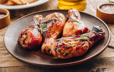 Chicken legs on brown plate with sauce and rosemary on wooden rustic background.