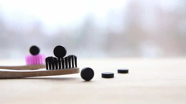 Pan view of black activated charcoal toothpaste tablets. Dental care concept. Natural ingredients, side view of bamboo toothbrush with black toothpaste tablet on brushes, blurred minimal background.