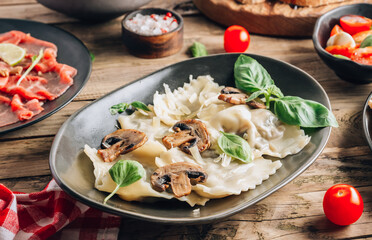 Italian cuisine - ravioli pasta with champignon mushrooms and parmesan cheese on black plate on wooden background.