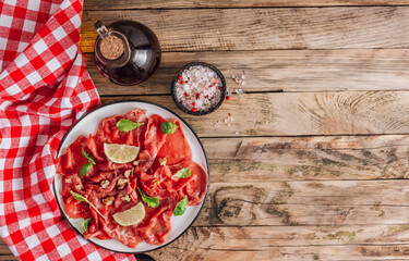 White plate with carpaccio of beef with baby arugula, lime and white wine on rustic wooden background.