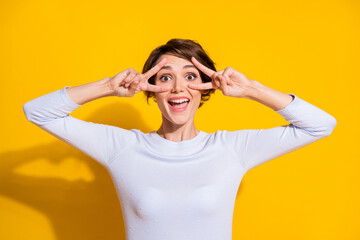 Photo portrait of excited girl showing two v-signs near eyes isolated on bright yellow colored background
