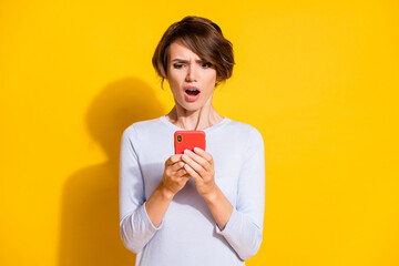 Photo portrait of upset girl holding phone in two hands isolated on bright yellow colored background