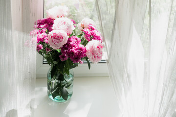 View of a bouquet of pink peonies and chrysanthemums in a vase on the window. Concept background, flowers, holiday.