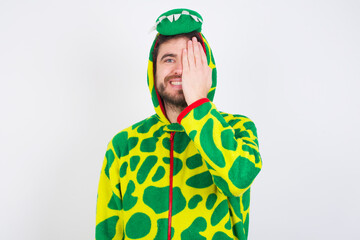 Fototapeta premium young caucasian man wearing a pajama standing against white wall covering one eye with her hand, confident smile on face and surprise emotion.