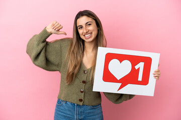 Young caucasian woman isolated on pink background holding a placard with Like icon with proud gesture