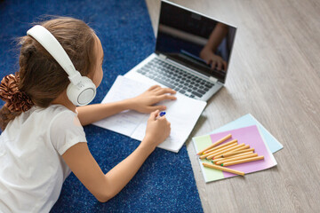 Fototapeta premium Pupil girl doing her homework online in front of a laptop monitor lying on the floor at home.