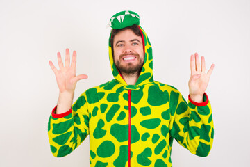 young caucasian man wearing a pajama standing against white wall showing and pointing up with fingers number nine while smiling confident and happy.