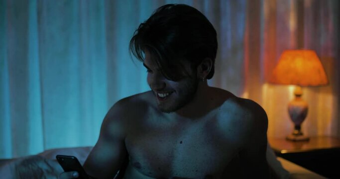 Ragazzo guarda il cellulare seduto sul letto 