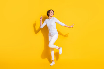 Fototapeta na wymiar Full length photo of cute funny young woman wear white shirt dancing pointing empty space isolated yellow color background