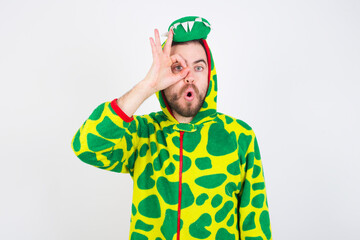Fototapeta premium young caucasian man wearing a pajama standing against white wall doing ok gesture shocked with surprised face, eye looking through fingers. Unbelieving expression.