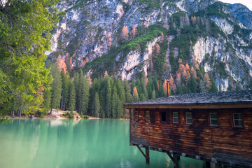 Sharp rock wall above turquoise water in Braies lake in Italian Alps. Wooden building standing on stilts above water.
