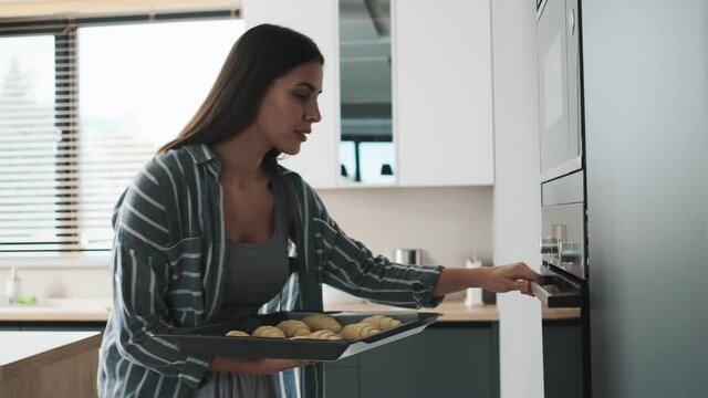 A good-looking young woman is baking croissants in the kitchen at home
