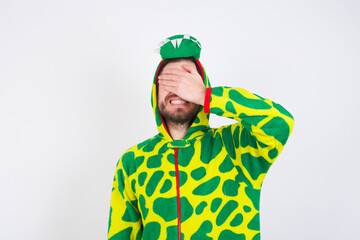 young caucasian man wearing a pajama standing against white wall smiling and laughing with hand on face covering eyes for surprise. Blind concept.