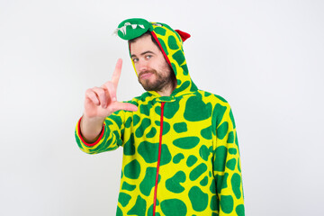 young caucasian man wearing a pajama standing against white background making fun of people with fingers on forehead doing loser gesture mocking and insulting.