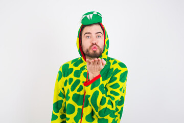 young caucasian man wearing a pajama standing against white background looking at the camera blowing a kiss with hand on air being lovely and sexy. Love expression.