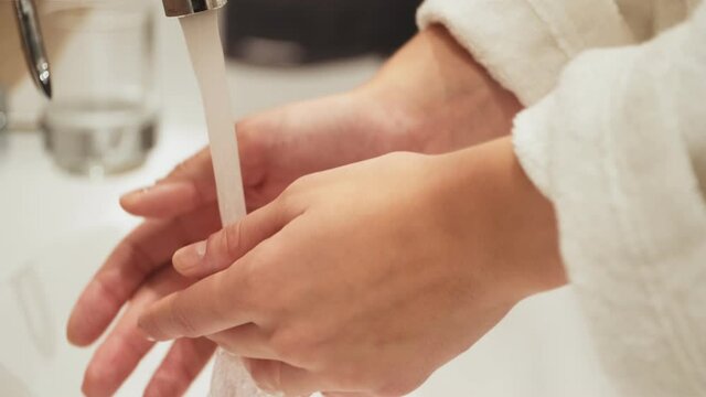 A close-up cropped view of a young woman is washing her hands in the bathroom