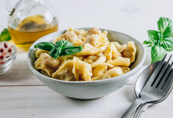 Tortellini with cheese sauce, basil leaves in bowl on white wooden background.