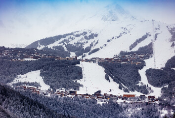 View of Courchevel ski resort slopes village, valley of Alps mountain over peaks and blue sky