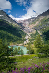 Fototapeta premium Scenic view of mountains against sky. Majestic waterfall leading from melting snow near Alp Grum. Rhaetian Railway track in foreground.