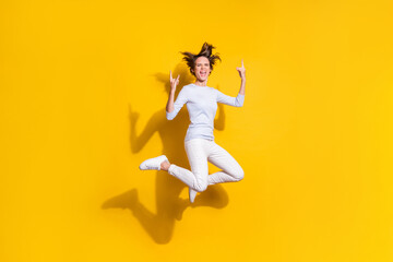 Fototapeta na wymiar Photo of lady jump open mouth raise horns signs wear white shirt trousers sneakers isolated yellow color background