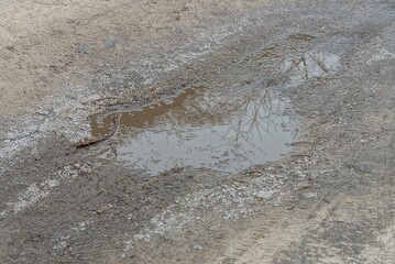 one puddle with brown muddy water and pieces of white ice on an earthen road outside