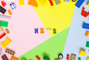 Words made of multi-colored wooden letters "news" on a multi-colored background, children's construction kit around. Top view.