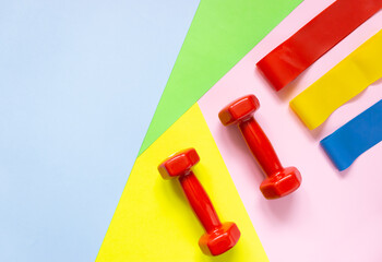 Red weights and rubber bands for sports on a colorful background. The concept of movement, sports, and a healthy lifestyle. Top view, free space for text.