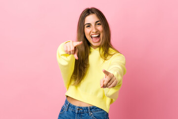 Young woman over isolated pink background surprised and pointing front