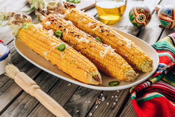 Grilled spicy corn cobs on white plate on rustic wooden background