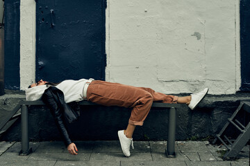 The girl lies on a metal bench. Fatigue and the aftermath of the party. Photo session in the city.