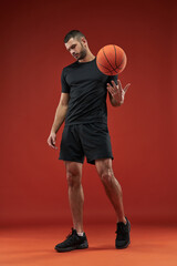 Naklejka premium Adorable strong muscular athlete posing at the camera with basketball in hand in the indoors