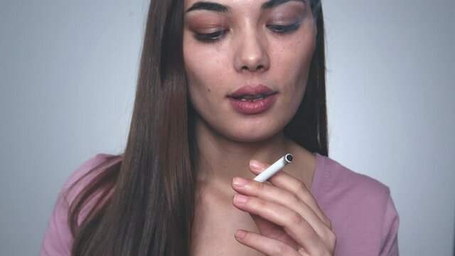 Beautiful woman smoking a cigarette on gray background.