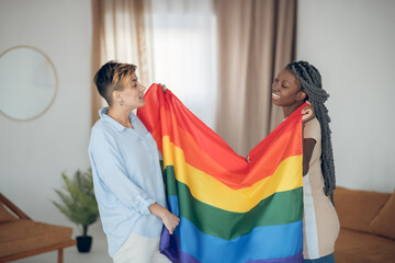Two young girls holding a rainbow flag and looking happy