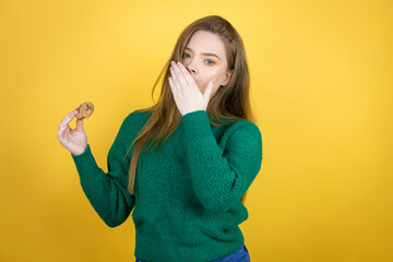 Young beautiful woman eating chocolate cookie over yellow background bored yawning tired covering mouth with hand. Restless and sleepiness.