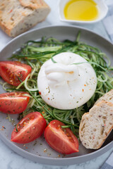 Salad with burrata cheese, cucumber and tomatoes served on a grey plate, close-up, vertical shot