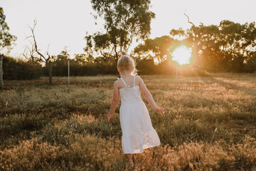 Fototapeta na wymiar Little blonde girl in field playing at sunset
