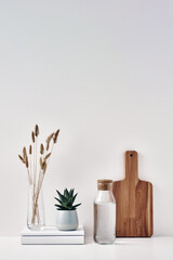 A transparent bottle, a vase with dried flowers on a white background, a houseplant and a wooden board. Eco-friendly materials in interior decor. Copy space, mock up.
