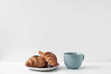 Blue mug and croissants on a white background. Eco-friendly and natural materials in the decor, dessert. Copy space, mock up.