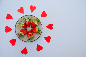 Festive blue background. Red paper hearts and fresh strawberries on a plate. Love. Valentine's Day. Food backgrounds. Creative greeting card. Flat lay, top view.