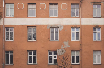 Fototapeta na wymiar A part of yellow brown building facade with windows and a tree in front of it. Street view cityscape of Klaipeda city in Litrhuania. Retro hipster faded style of processing. Grey and gloomy mood