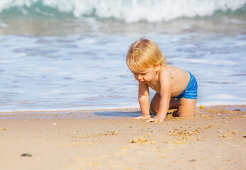 Fototapeta na wymiar Little blond toddler boy crawl on the sand beach near sea waves