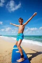 Boy training to ride surfboard on the beach during lesson practicing with his board in cute sunglasses