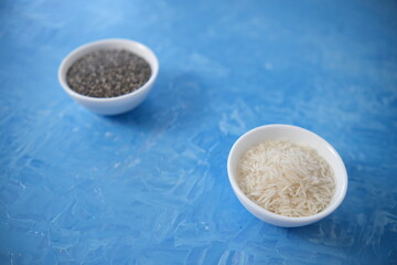 Rice and chia seeds are organic food for a healthy diet. In a round bowl. Two white cups. The blue background is painted with oil paints.